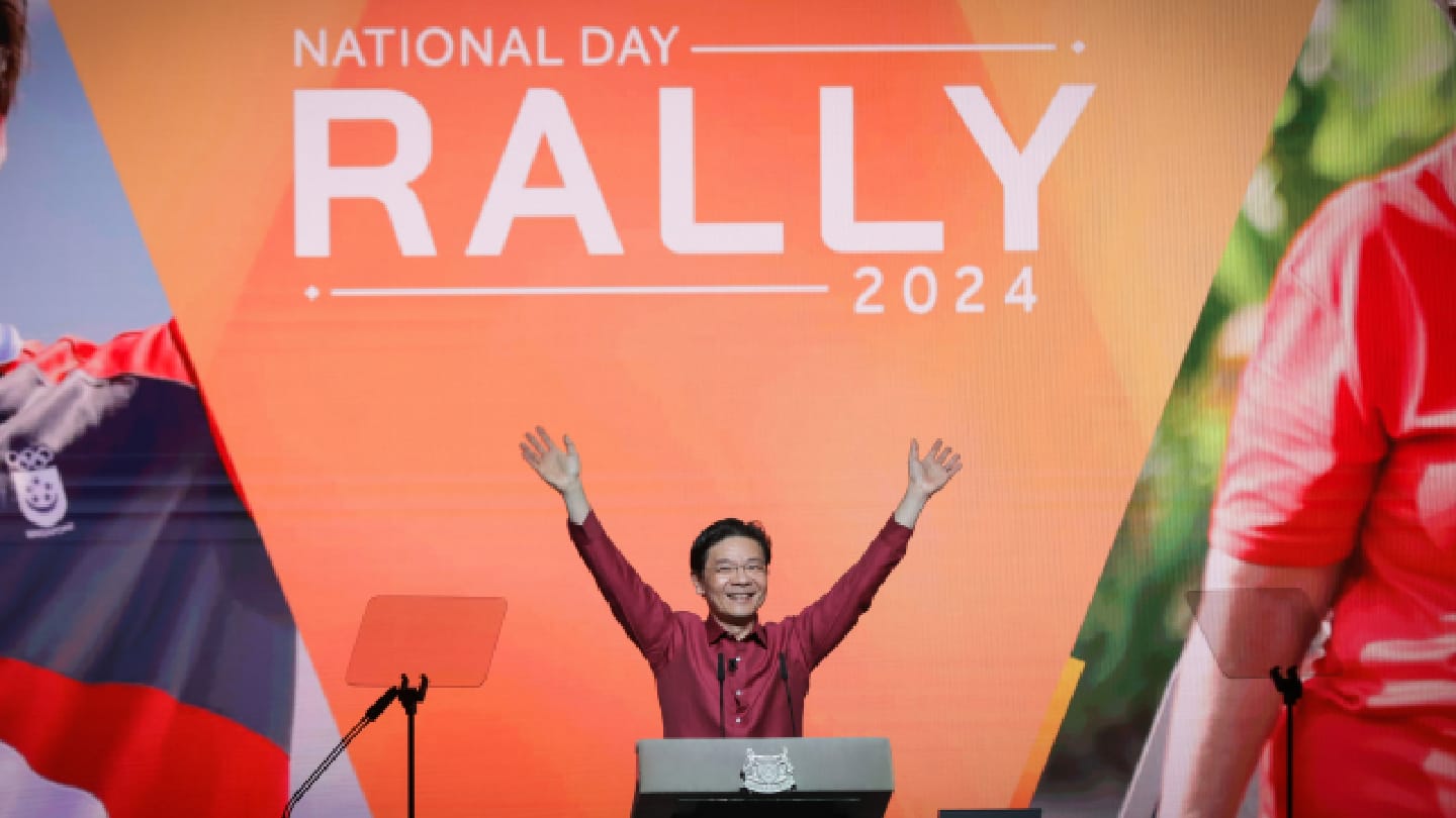 Lawrence Wong raises arms on stage before "National Day Rally 2024" graphic.